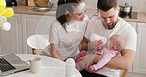 Mother with laptop and father feeds baby girl.