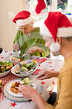 Mother in law and son in law wearing santa hats sitting at christmas table and eating