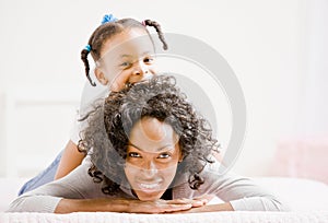 Mother lays on bed with playful daughter