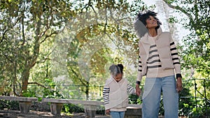 Mother leading little daughter by hand walking green park. Girl holding mom hand