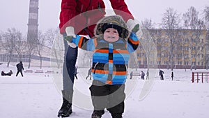 Mother leads the hands of a small smiling baby in the snow in the park. The first steps of the child. Parental care
