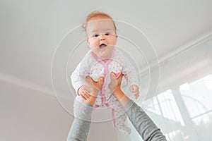 A mother lifted the happy child in her arms. Bottom view. White interior. The concept of motherhood and happy childhood