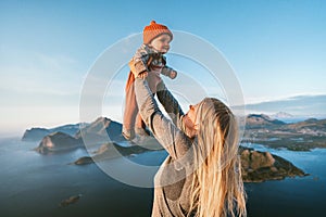 Mother lifting up infant baby family traveling in Norway summer vacations in Lofoten islands woman with child