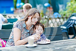 Mother and little adorable kid girl drinking coffee in outdoor c