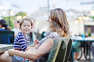 Mother and little adorable kid girl drinking coffee in outdoor c