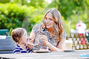 Mother and little adorable kid girl drinking coffee in outdoor c