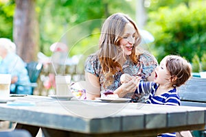 Mother and little adorable kid girl drinking coffee in outdoor c