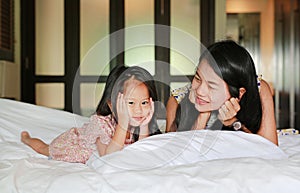 Mother and little asian girl looking camera and lying on bed