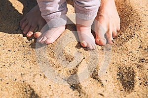 Mother and little baby feet on beach sand.