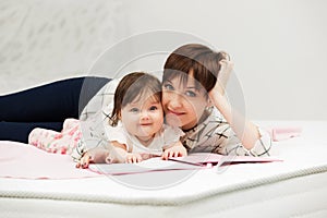 Mother and little baby girl reading a book on bed