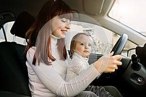 Mother with little baby girl sitting in front seat and driving car together. Child in danger, no safety on the road