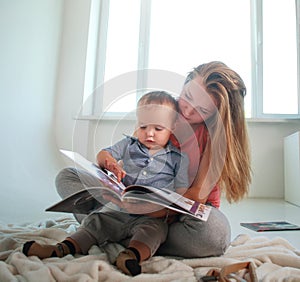 Mother with a little baby son in a room reading book at home