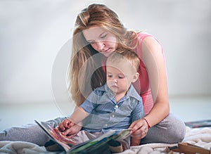 Mother with little baby son in room reading book at home