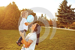 Mother with a little boy in her arms is smiling in the summer park.