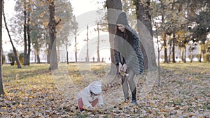 Mother and little child in an autumn park throw dry leaves up, happy family, live fun with mom, nature walk. Slow motion