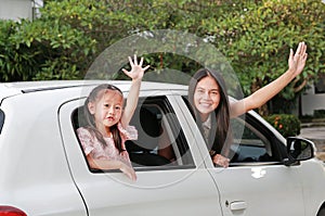 Mother and little child girl sitting on a car looking camera and waving goodbye. Holiday concept