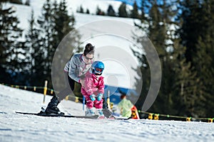 Mother and little child skiing in Alps mountains. Active mom and toddler kid with safety helmet, goggles and poles.