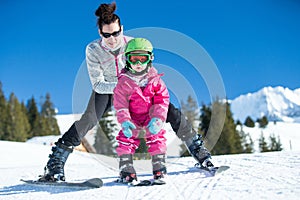 Mother and little child skiing in Alps mountains. Active mom and toddler kid with safety helmet, goggles and poles.