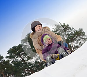 Mother with little child sliding in the snow