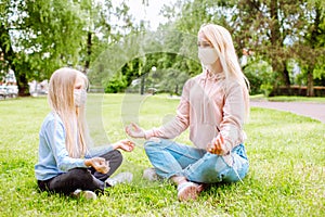 Mother and little daugher on the park wearing protective masks. Mom teaching girl yoga. Family, mothers day, covid pandemic