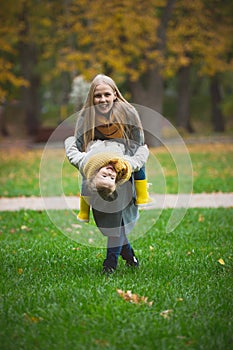 Mother and little daughter blonde with Teddy bear have fun and playing on green grass in autumn park