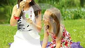 Mother with little daughter blowing soap bubbles on the meadow