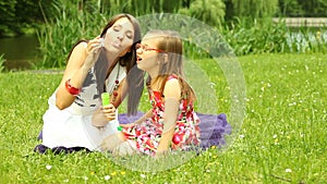 Mother with little daughter blowing a soap bubbles outdoor