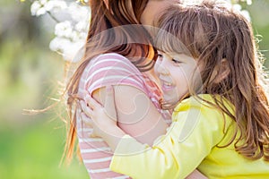 Mother and little daughter with bunny ears standing under a blooming cherry tree at sunny spring Easter day