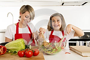 Mother and little daughter cooking together with cook apron preparing salad at home kitchen