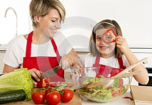 Mother and little daughter cooking together with cook apron preparing salad at home kitchen