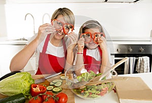 Mother and little daughter cooking together with cook apron preparing salad at home kitchen