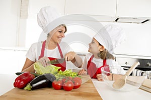 Mother and little daughter cooking together with hat apron preparing salad at home kitchen