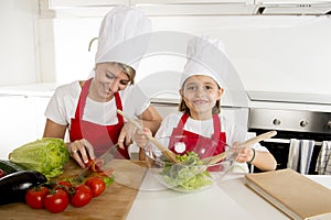 Mother and little daughter cooking together with hat apron preparing salad at home kitchen