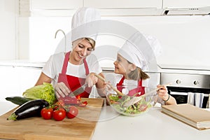 Mother and little daughter cooking together with hat apron preparing salad at home kitchen