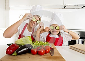 Mother and little daughter cooking together playing with cucumber slices on the eyes