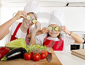 Mother and little daughter cooking together playing with cucumber slices on the eyes