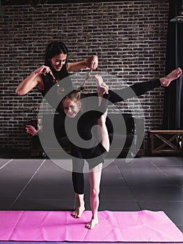 Mother and little daughter doing standing split leg stretching exercise keeping balance