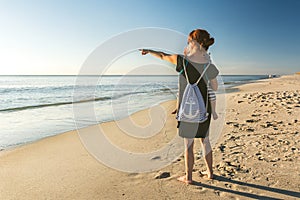 Mother with little daughter on her arm at the beach pointing towards the ocean