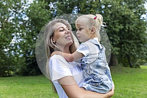 A mother with a little daughter in her arms laughs and hugs in a summer park. Love and tenderness