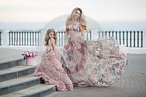 Mother and little daughter in pink ball gowns outdoors in summer near the palace.