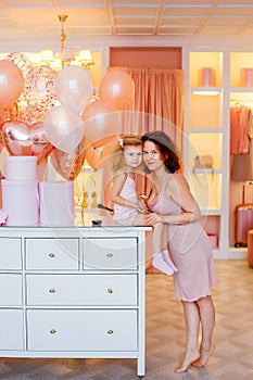 A mother and a little daughter in pink pajamas are doing makeup in the bedroom