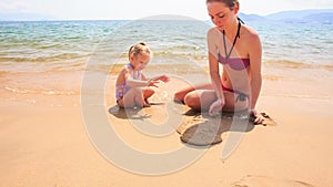 Mother Little Daughter Play with Sand on Beach of Azure Sea