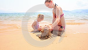 Mother Little Daughter Play with Sand on Beach of Azure Sea