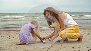 Mother with little daughter playing with pebble stones on the beach