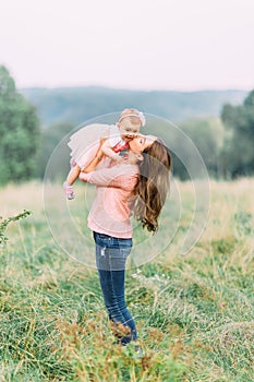 Mother and little daughter playing together in a park. Happy cheerful family. Mother and baby kissing, laughing and