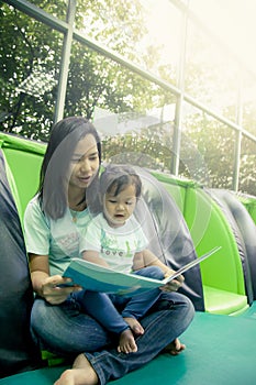 Mother and little daughter reading book together in library