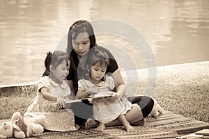 Mother and little daughter reading book together in the park