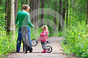 Mother and little daughter riding bikes in summer forest