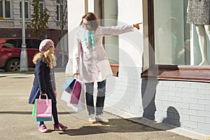 Mother and little daughter with shopping bags. Outdoor, background city, store windows.