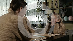 mother and little daughter sit in a cafe and talk sweetly, smile